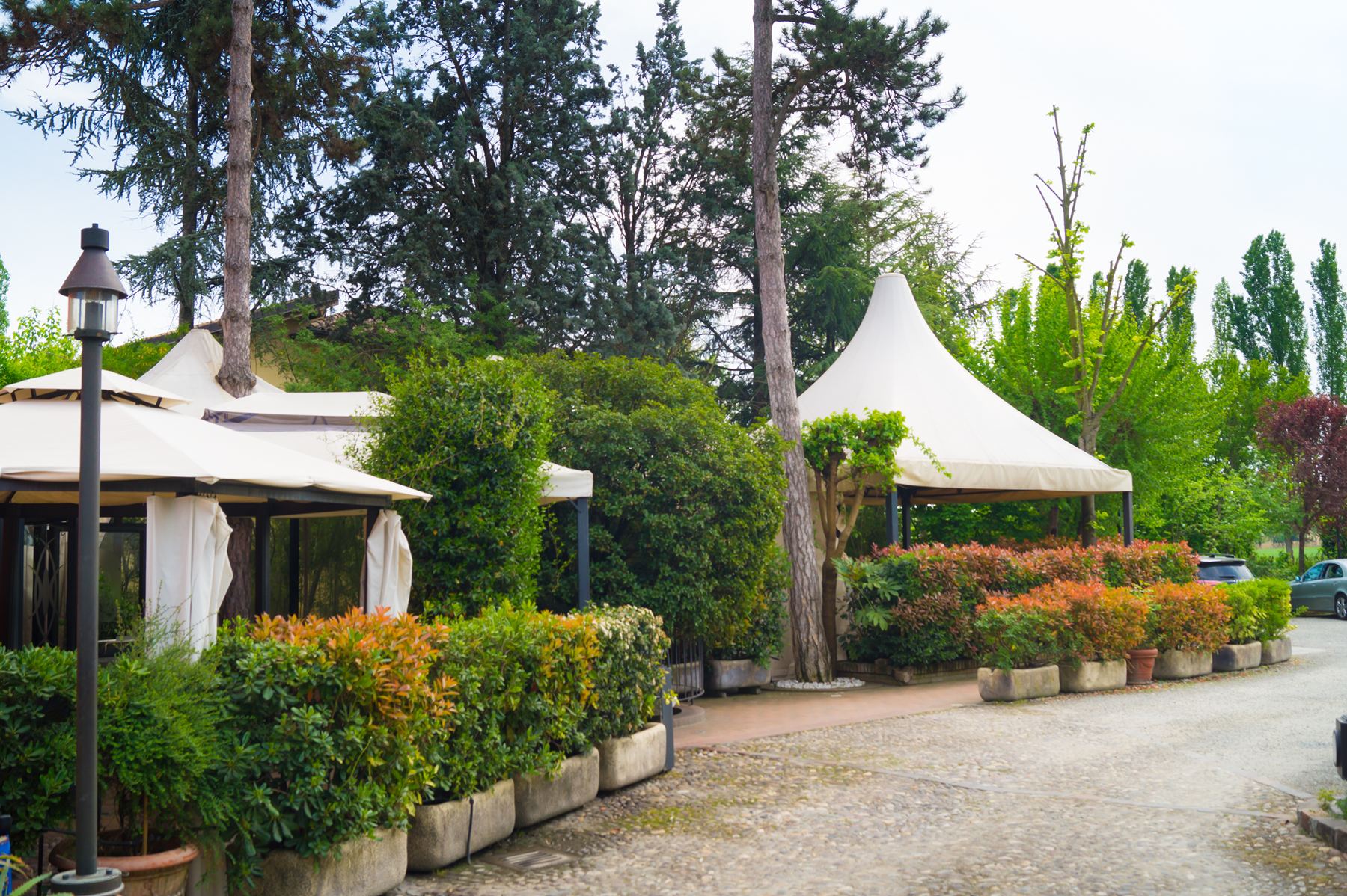 Il giardino estivo del Patriarca con i gazebo color crema tra pini e siepi fiorite