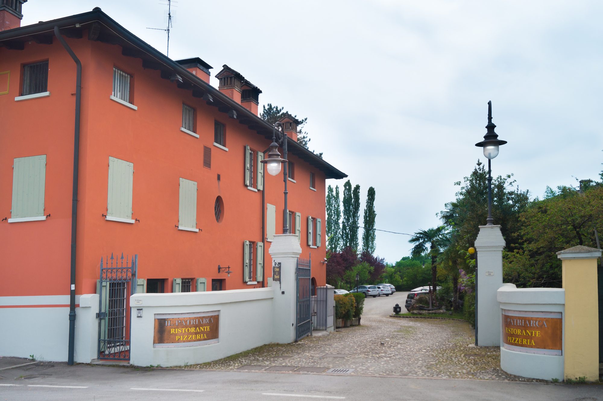 Il vialetto in ciottoli che porta alla casa color cotto del Ristorante Il Patriarca, tra il giardino e i lampioni